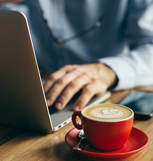 A man is working on a laptop with a cup of coffee