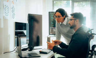 Zwei Personen sitzen vor einem Bildschirm und diskutieren über die Kriterien um den richtigen IT-Partner auszuwählen